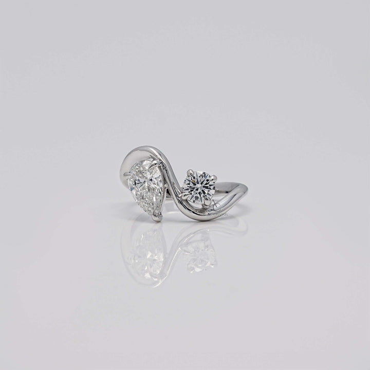 Pear and round diamond bypass ring on a reflective surface.