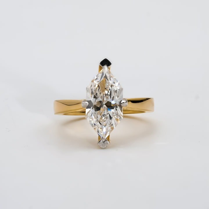 A yellow gold engagement ring featuring a marquise-cut diamond at the center, secured by six prongs. The diamond’s elongated shape adds brilliance and elegance to the simple, polished gold band.