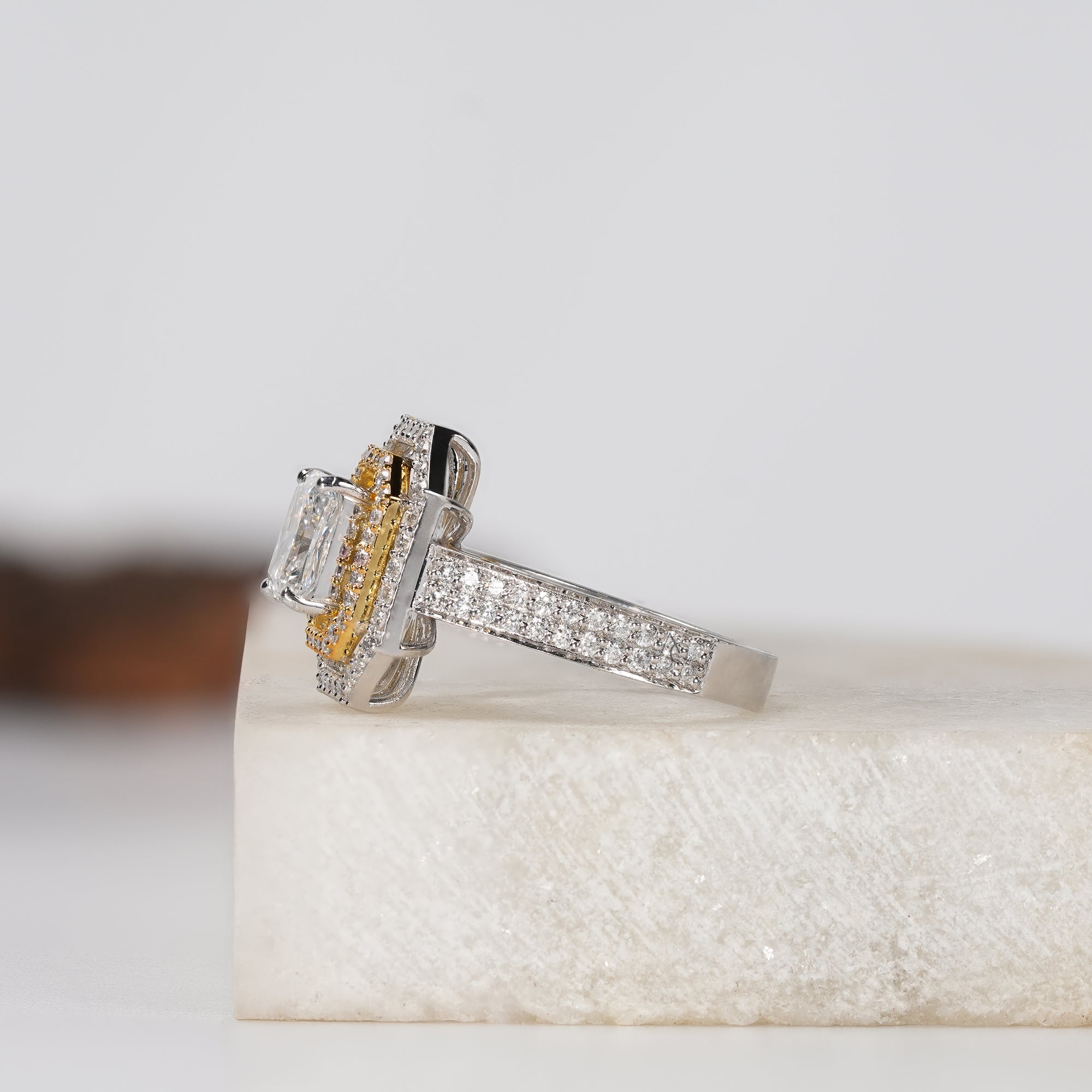 engagement ring with a rectangular radiant-cut center stone, surrounded by a double halo of small diamonds, set on a pavé diamond band in white and yellow gold,