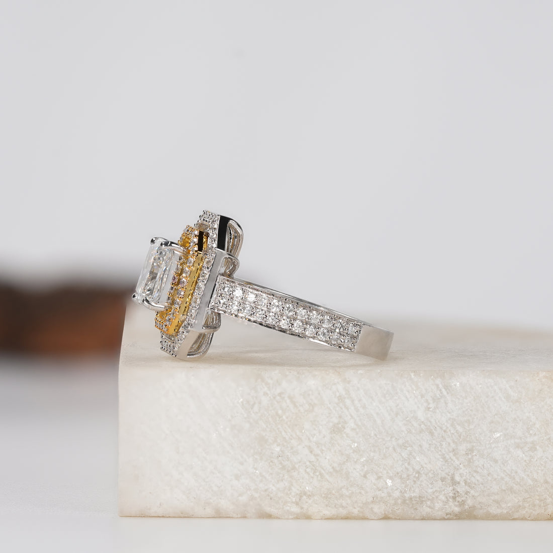 engagement ring with a rectangular radiant-cut center stone, surrounded by a double halo of small diamonds, set on a pavé diamond band in white and yellow gold,