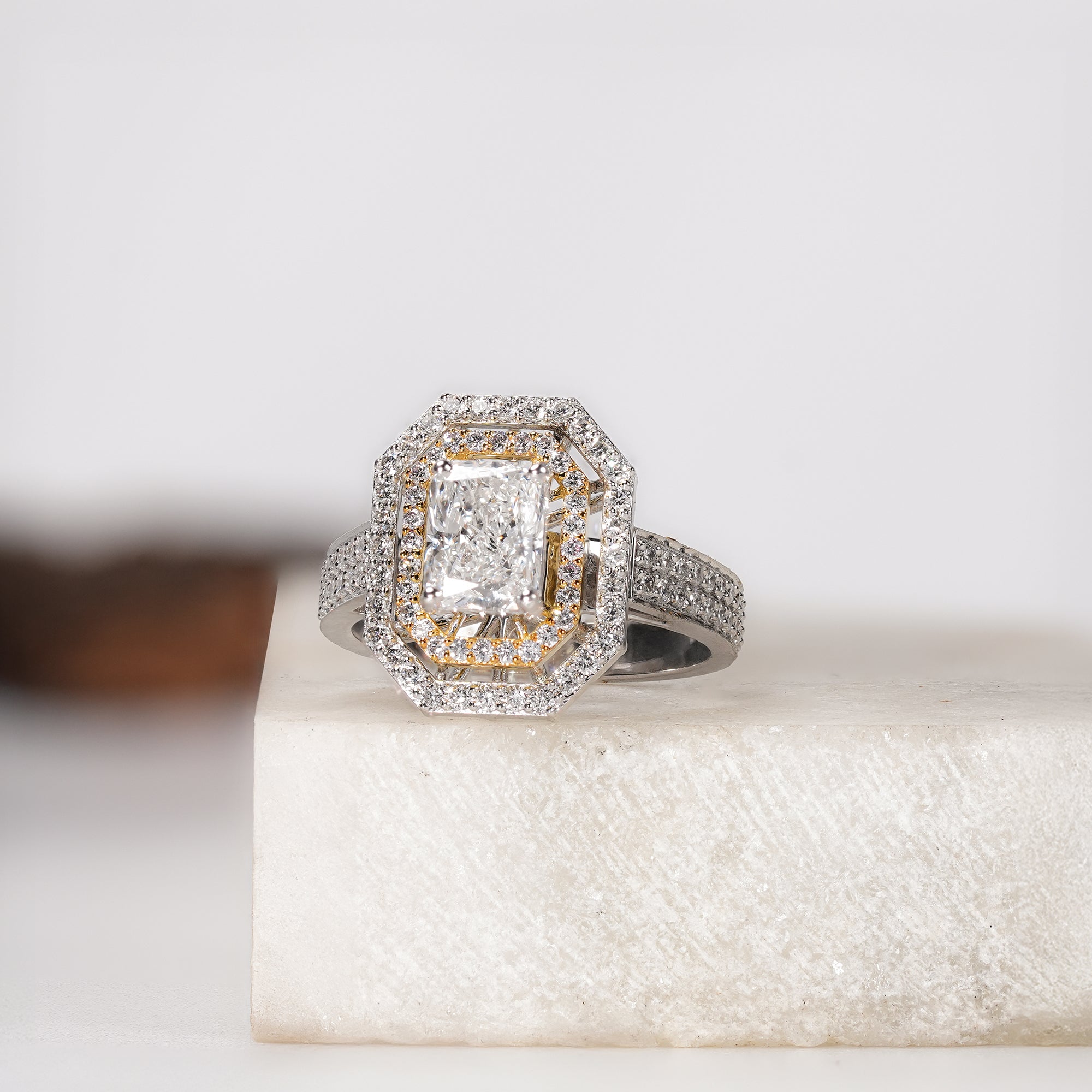 Radiant-cut diamond ring with double halo and pavé band on a light stone surface