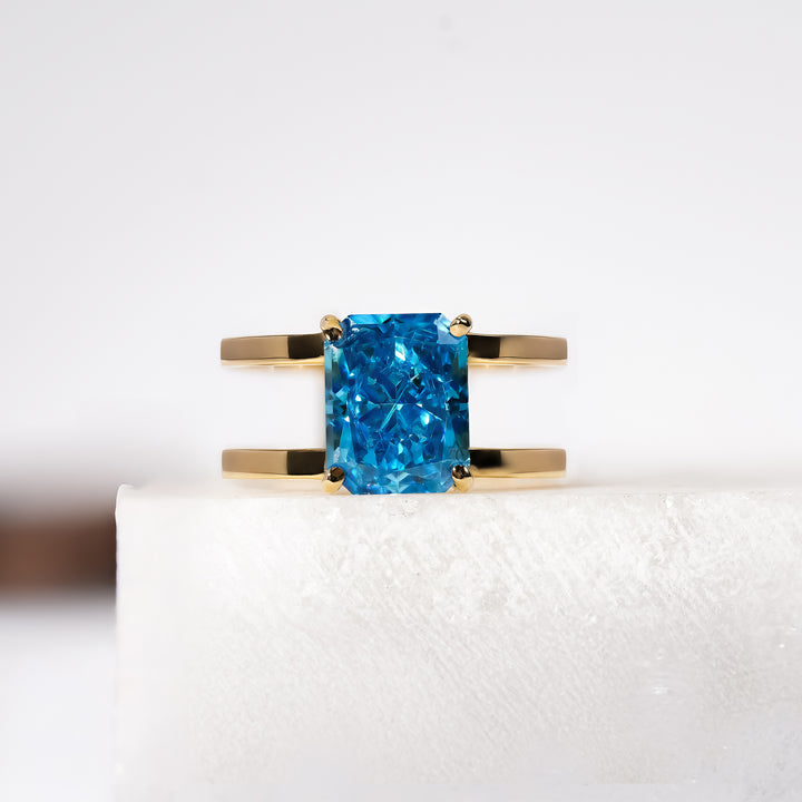 A gold ring featuring a radiant rectangular-cut blue gemstone