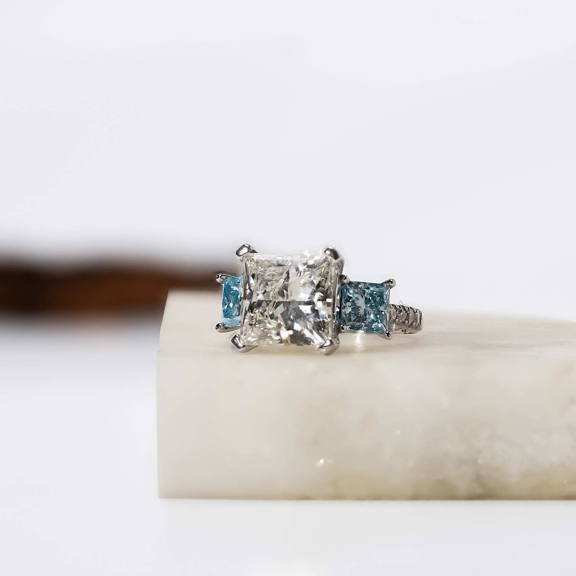 Elegant engagement ring featuring a square princess white diamond flanked by two sky-blue diamonds in white gold.