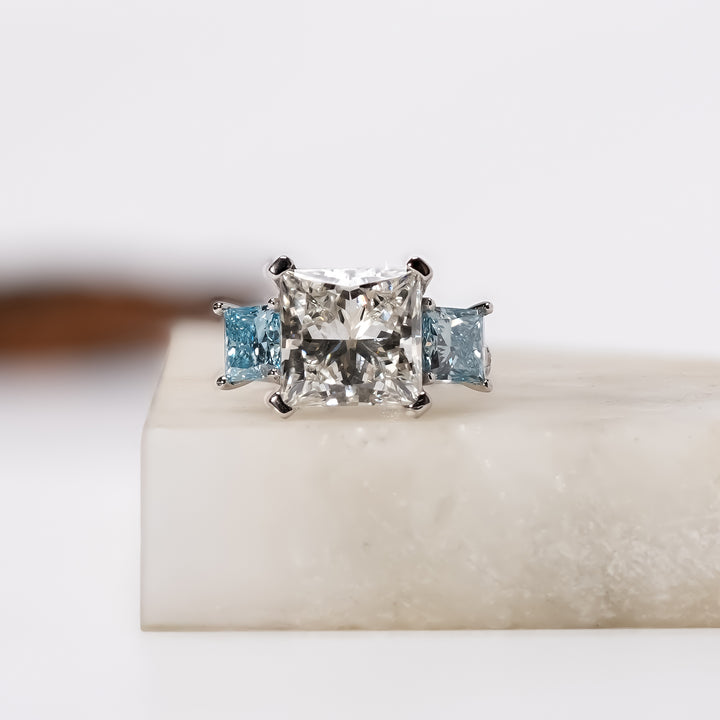 Three-stone ring with a princess-cut center diamond and two blue princess-cut side diamonds set in a white gold band