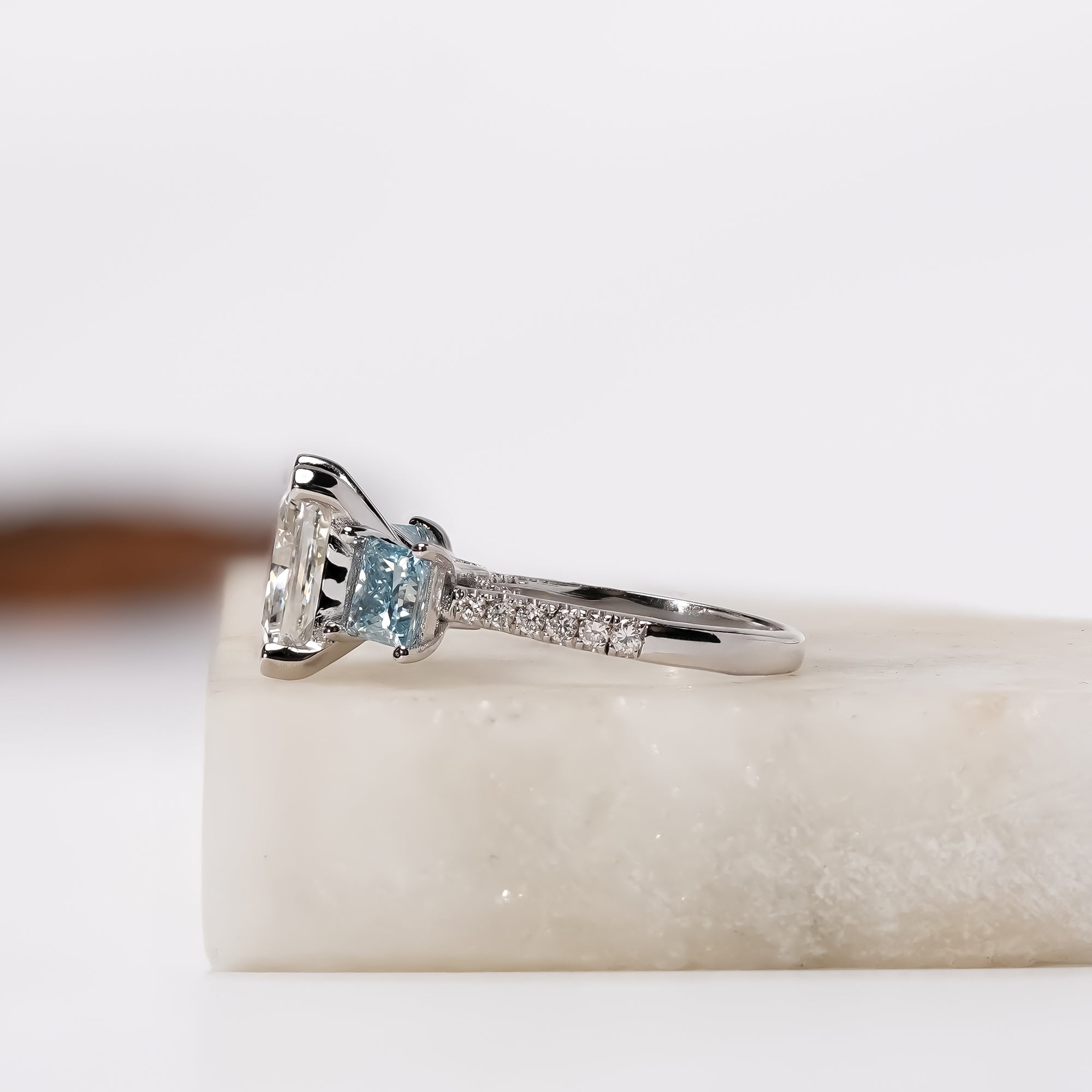 A white gold three-stone diamond ring with a princesscut center stone and two square-cut blue diamonds.