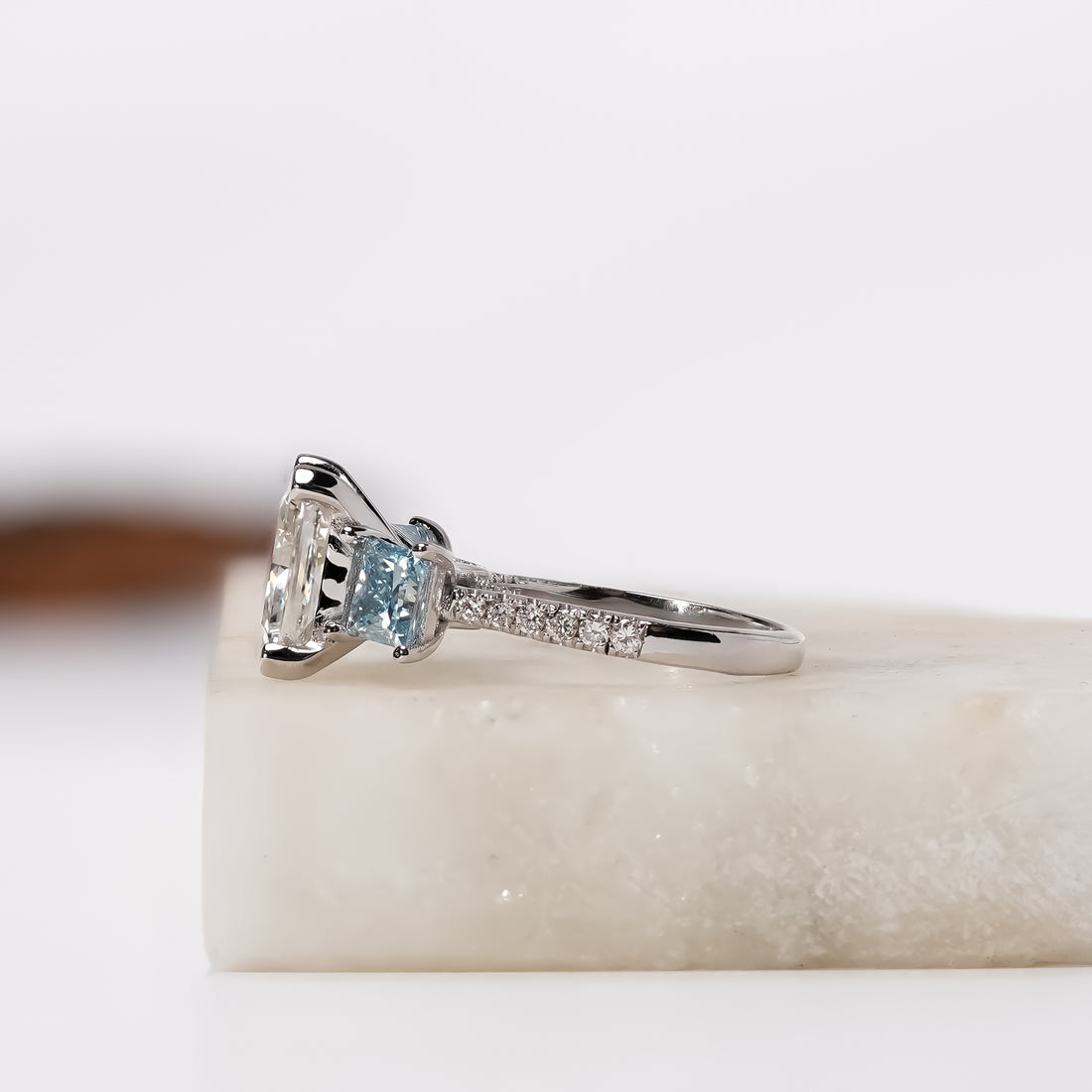 A white gold three-stone diamond ring with a princesscut center stone and two square-cut blue diamonds.