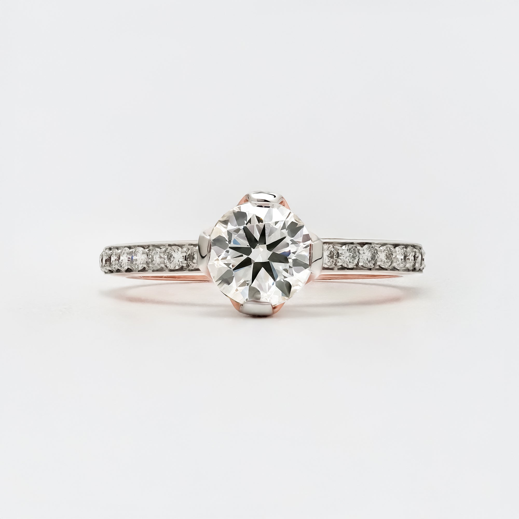 A solitaire engagement ring featuring a round brilliant-cut diamond set in a white gold band with small pavé-set diamonds along the shank.