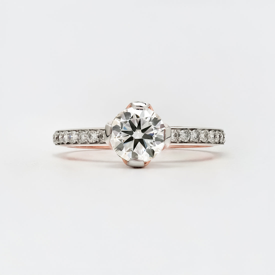 A solitaire engagement ring featuring a round brilliant-cut diamond set in a white gold band with small pavé-set diamonds along the shank.