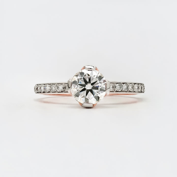 A solitaire engagement ring featuring a round brilliant-cut diamond set in a white gold band with small pavé-set diamonds along the shank.