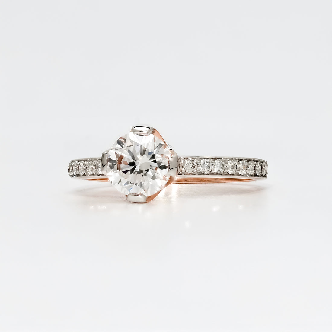 A round brilliant-cut diamond engagement ring with a pavé diamond band in a polished rose gold setting.