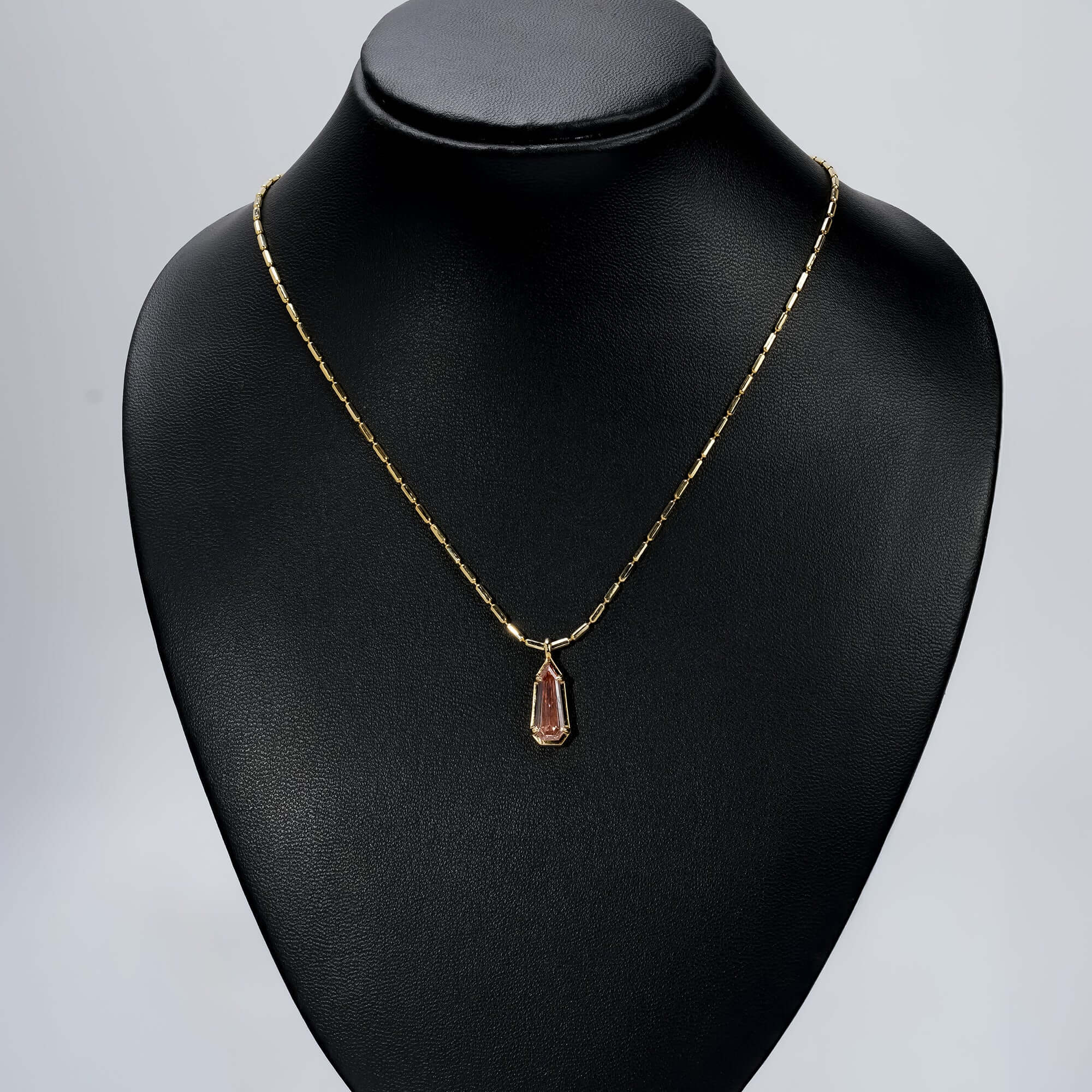 Gold chain necklace with an elongated pink gemstone pendant, a luxurious, timeless look.