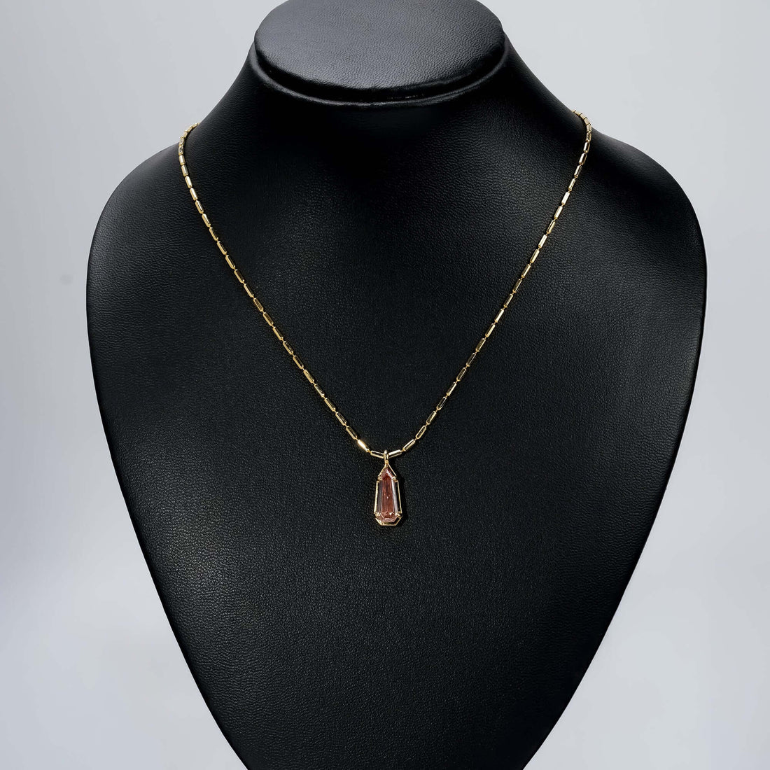 Gold chain necklace with an elongated pink gemstone pendant, a luxurious, timeless look.