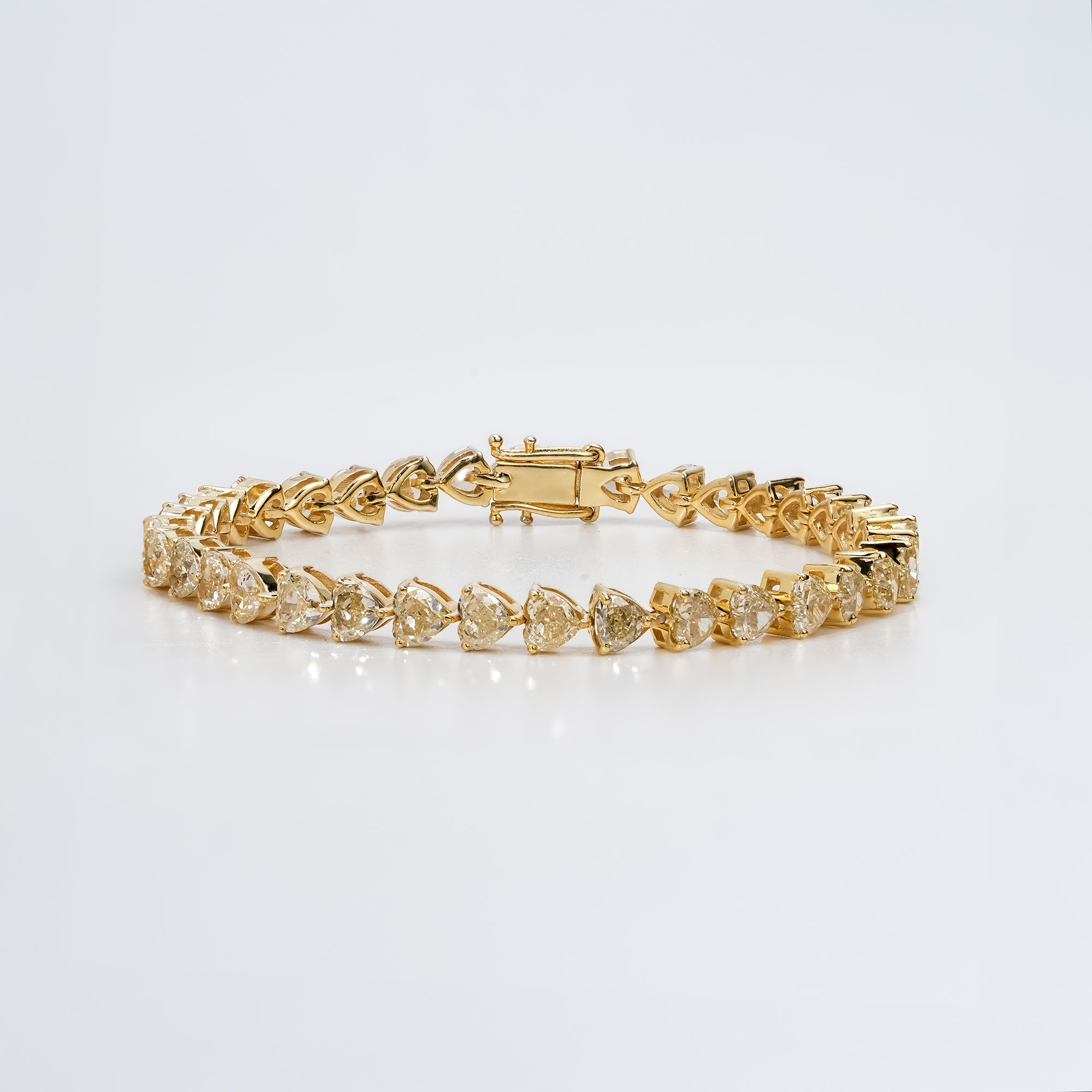 Gold diamond tennis bracelet with heart cut stones in a prong setting, featuring a secure clasp and polished finish for a luxurious, elegant design.