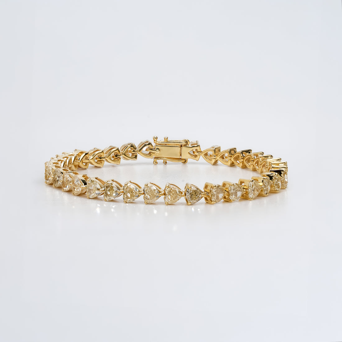 Gold diamond tennis bracelet with heart cut stones in a prong setting, featuring a secure clasp and polished finish for a luxurious, elegant design.