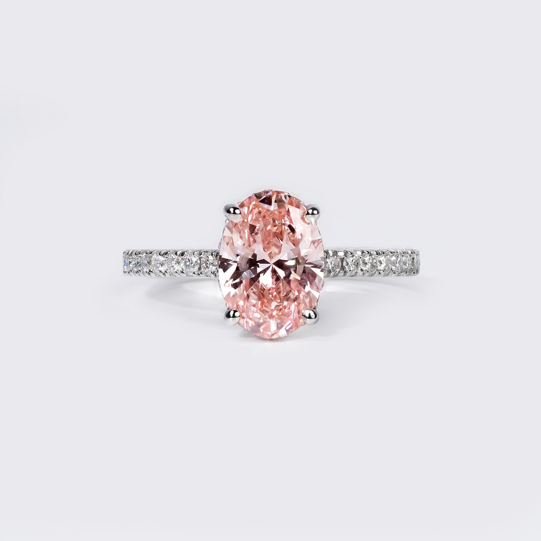 An oval-cut pink diamond ring set in a white gold band adorned with small pavé-set white diamonds.