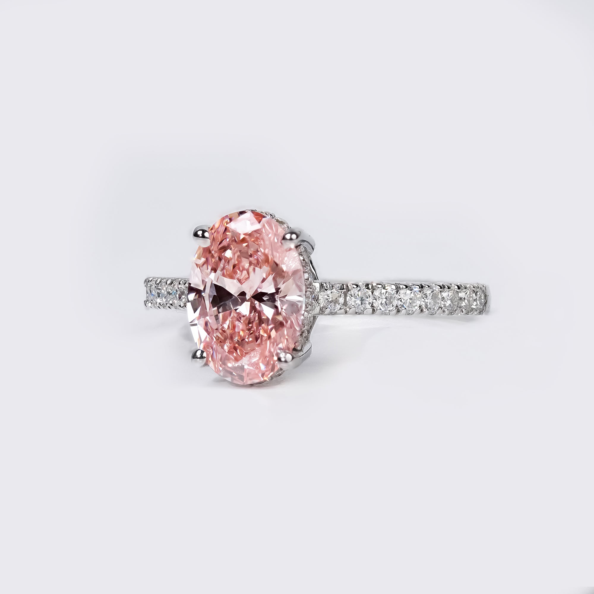 An elegant oval pink diamond ring with a pavé diamond band in a polished white gold setting.