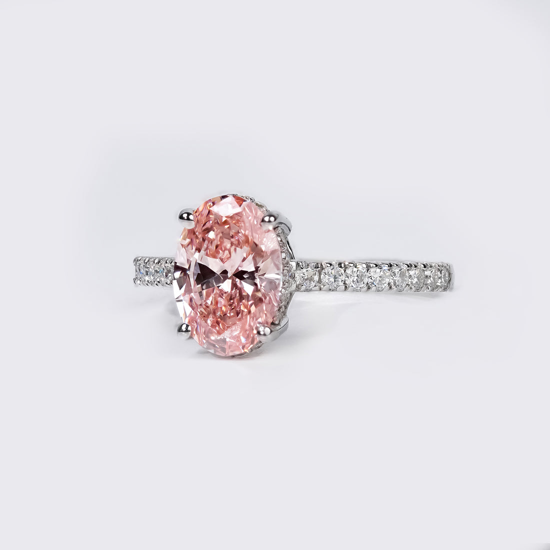 An elegant oval pink diamond ring with a pavé diamond band in a polished white gold setting.