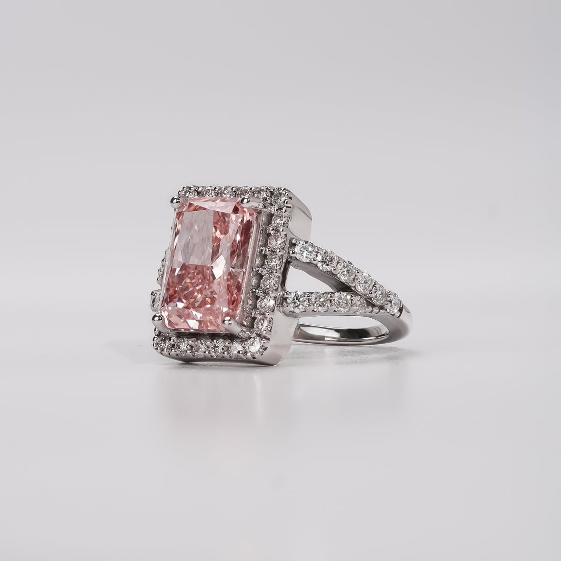 Luxury engagement ring featuring a rectangular pink diamond centerpiece framed by a halo of brilliant white diamonds on a sparkling split band.