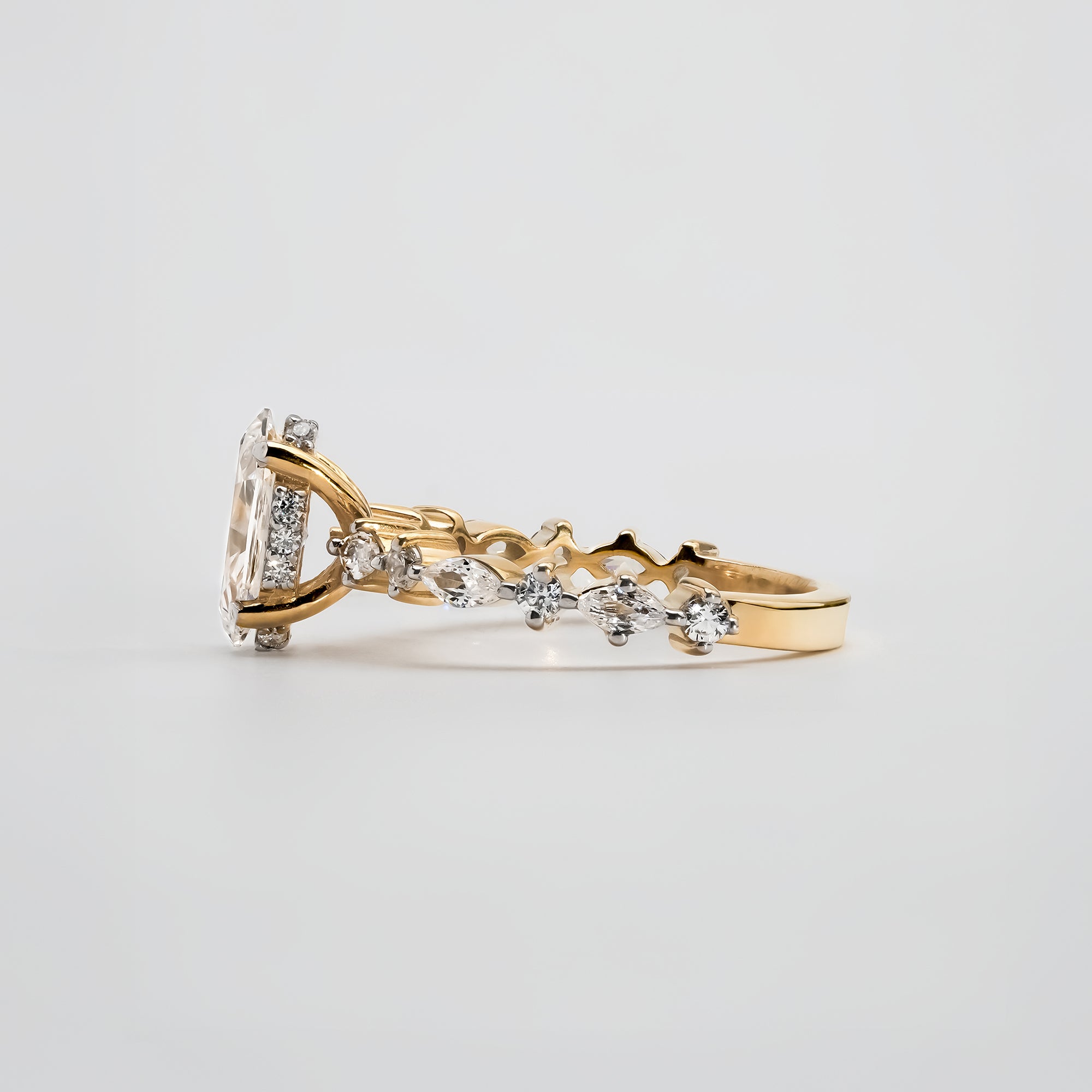 A yellow gold ring with a marquise-cut diamond centerpiece set in six prongs. The band features alternating marquise and round-cut diamonds in a woven design, adding sparkle and sophistication to the elegant setting.