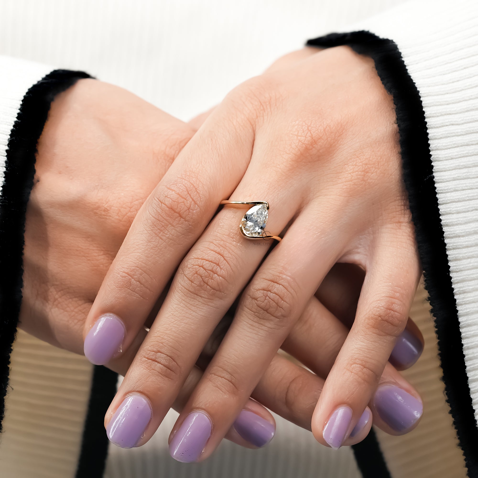pear-shaped diamond engagement ring with a smooth, sculptural yellow gold band that wraps around the stone