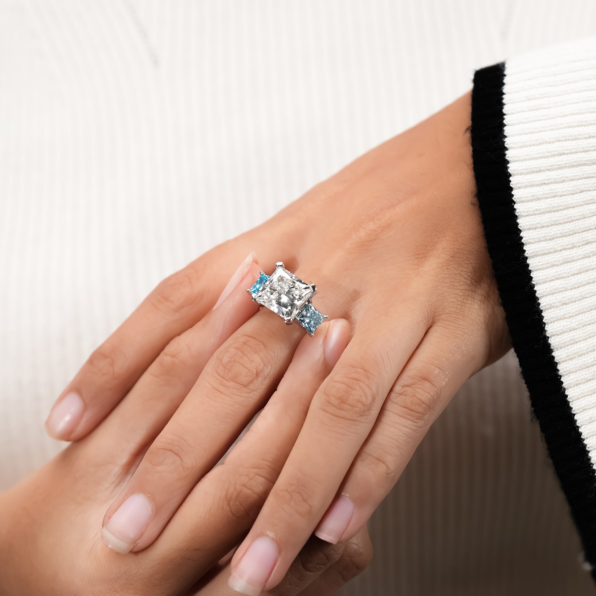 Luxury white gold ring showcasing a princess diamond center stone with vivid blue side diamonds