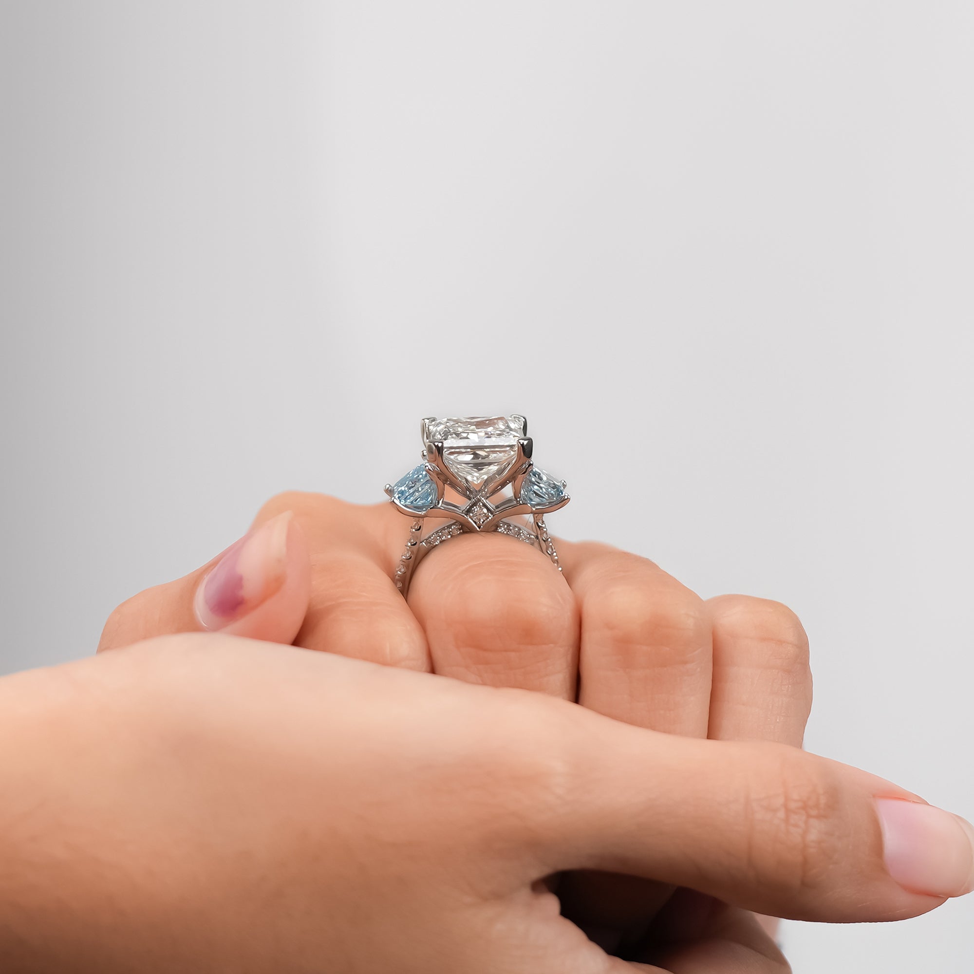 White gold three-stone engagement ring with princess-cut diamond and two blue side stones.