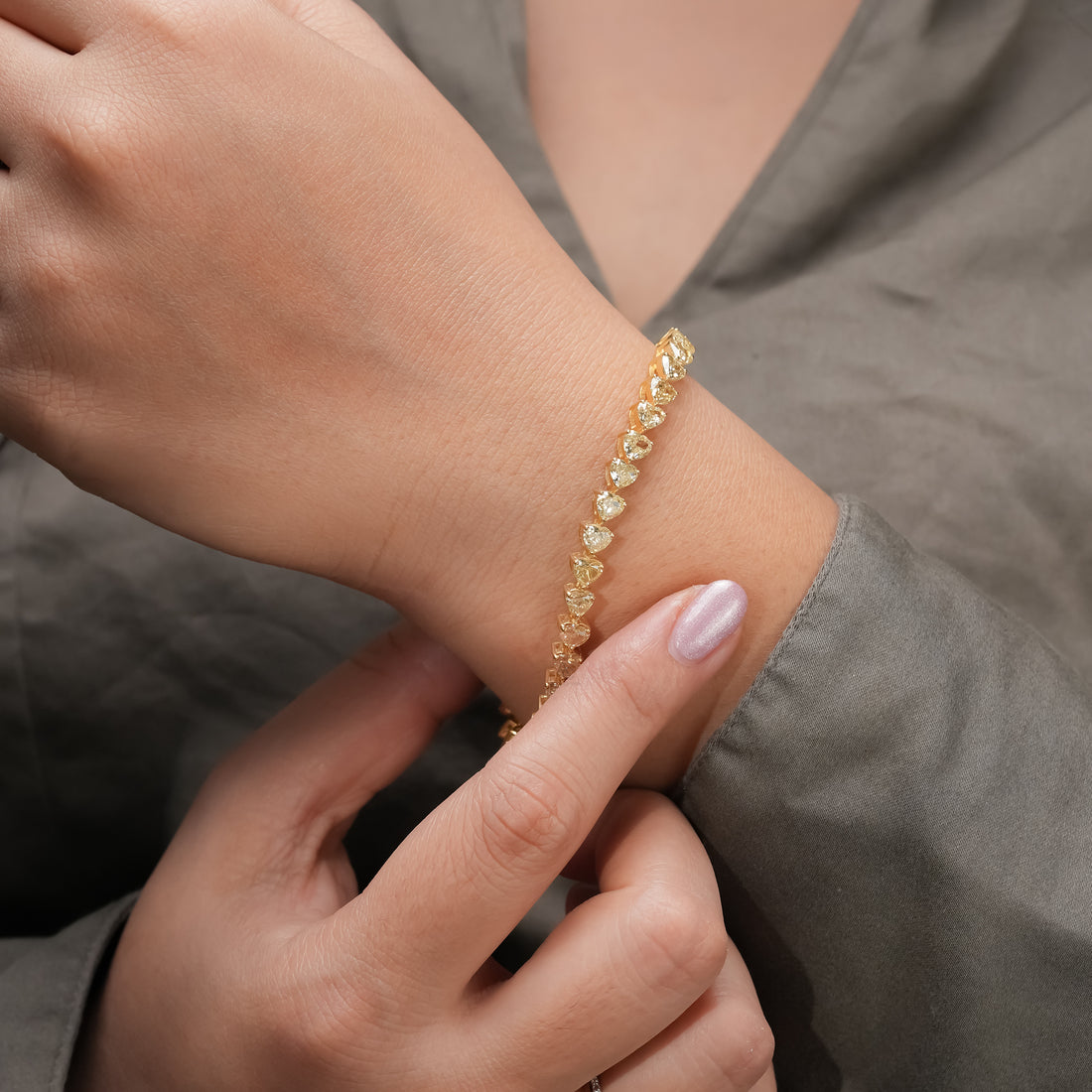 A gold bracelet featuring heart-shaped diamonds in a continuous line, each gemstone set in a secure gold prong setting. The bracelet’s lustrous finish highlights its luxurious craftsmanship.