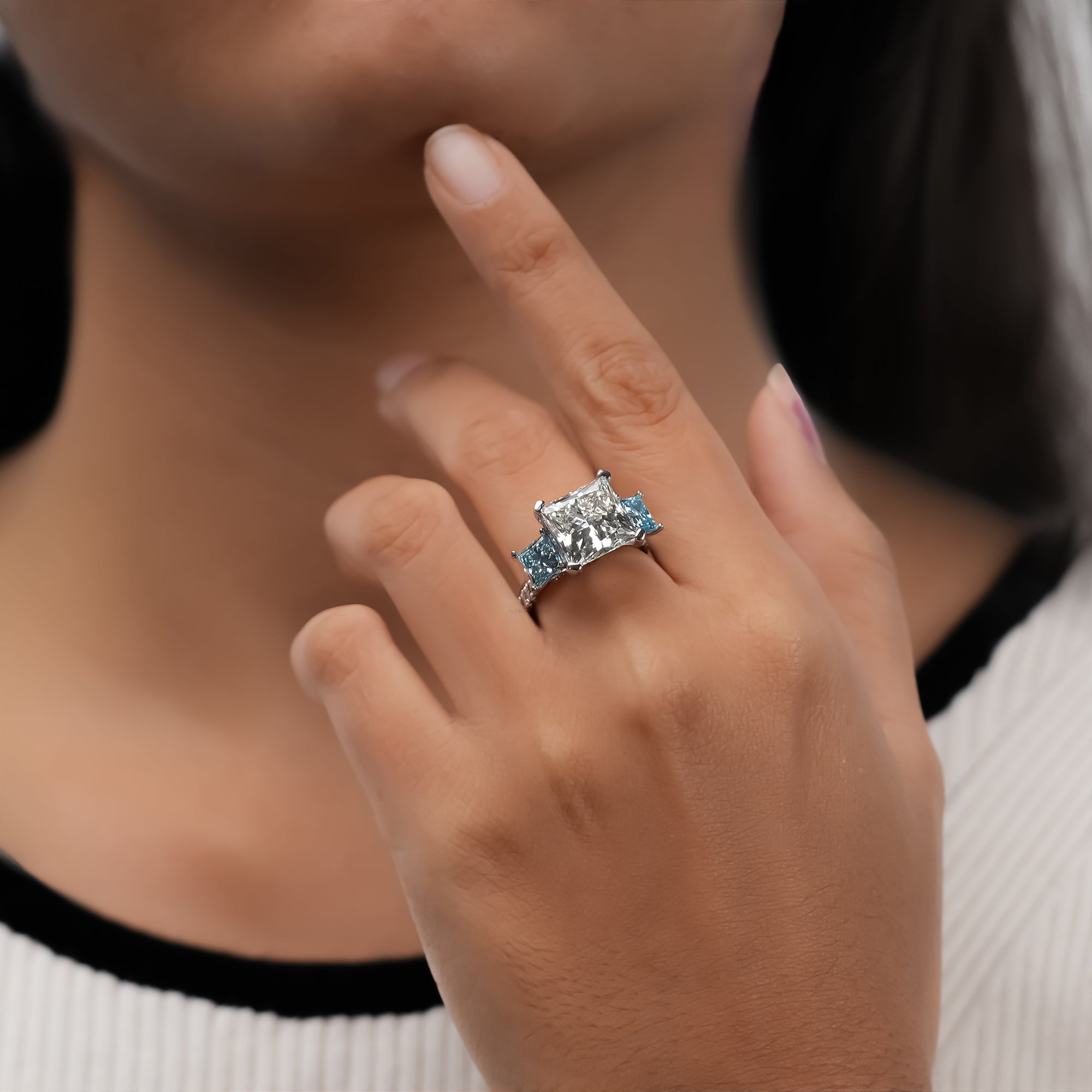 Luxury three-stone white gold ring with princess-cut diamond center and blue accent diamonds.