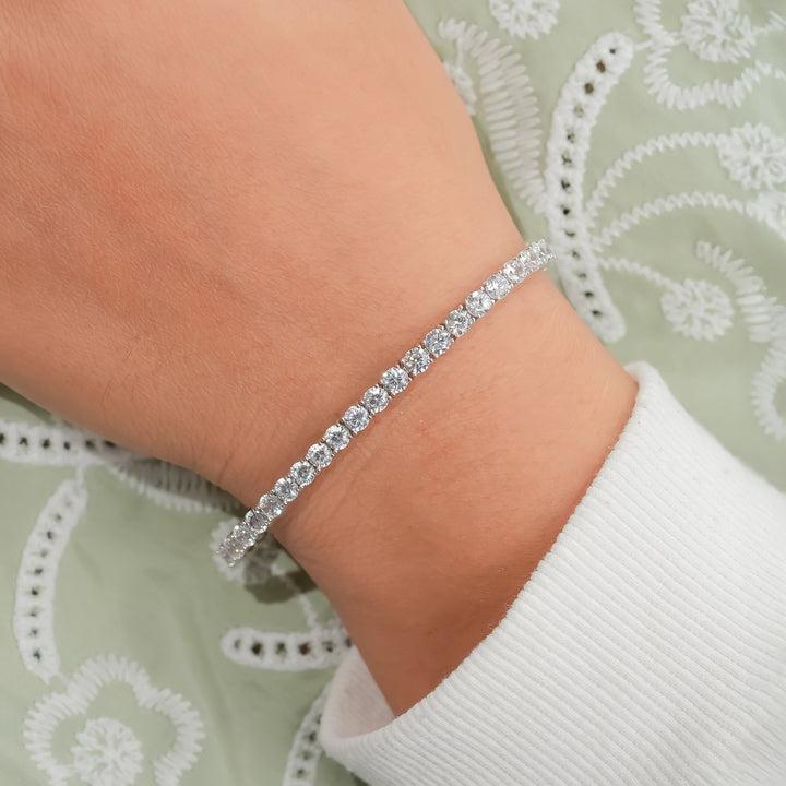 A woman's wrist wearing a delicate diamond tennis bracelet, featuring round-cut diamonds set in a continuous silver band.