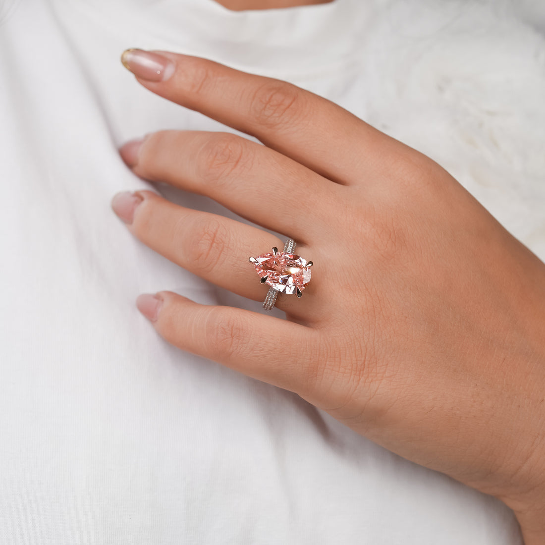 A radiant pear-shaped pink stone rests in a rose gold setting, its soft blush hue symbolizing affection and tenderness, framed by a sparkling band of diamonds.