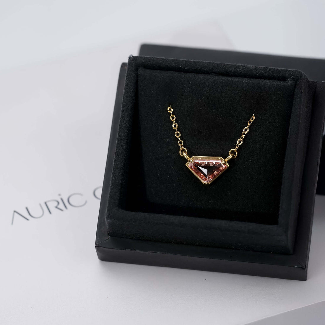 Gold necklace with a kite-shaped pink gemstone pendant, a luxurious and stylish presentation.