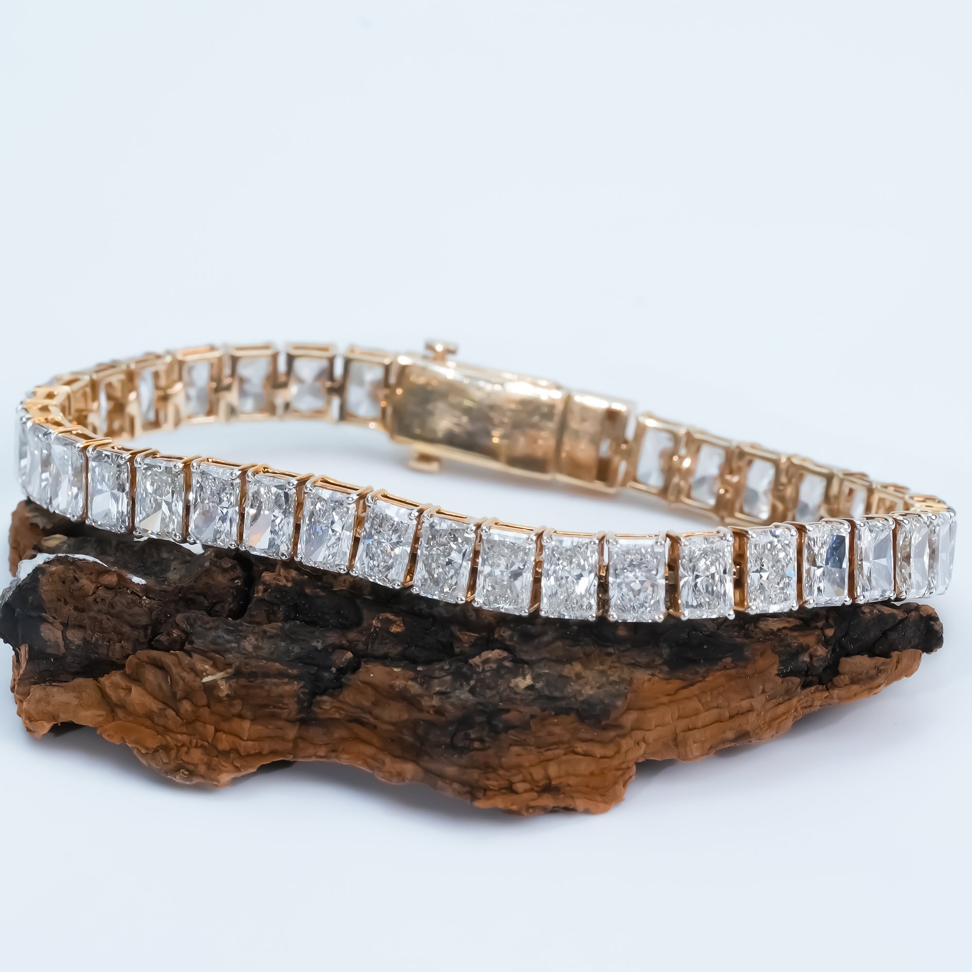Gold diamond tennis bracelet with radiant cut stones in a sleek channel setting, displayed on a light  to emphasize its luxurious design.