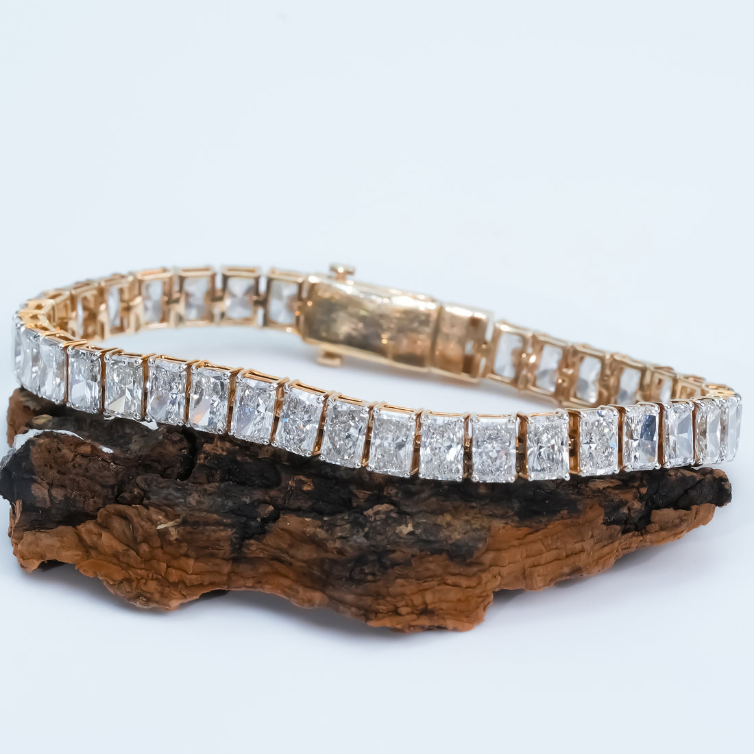 Gold diamond tennis bracelet with radiant cut stones in a sleek channel setting, displayed on a light  to emphasize its luxurious design.