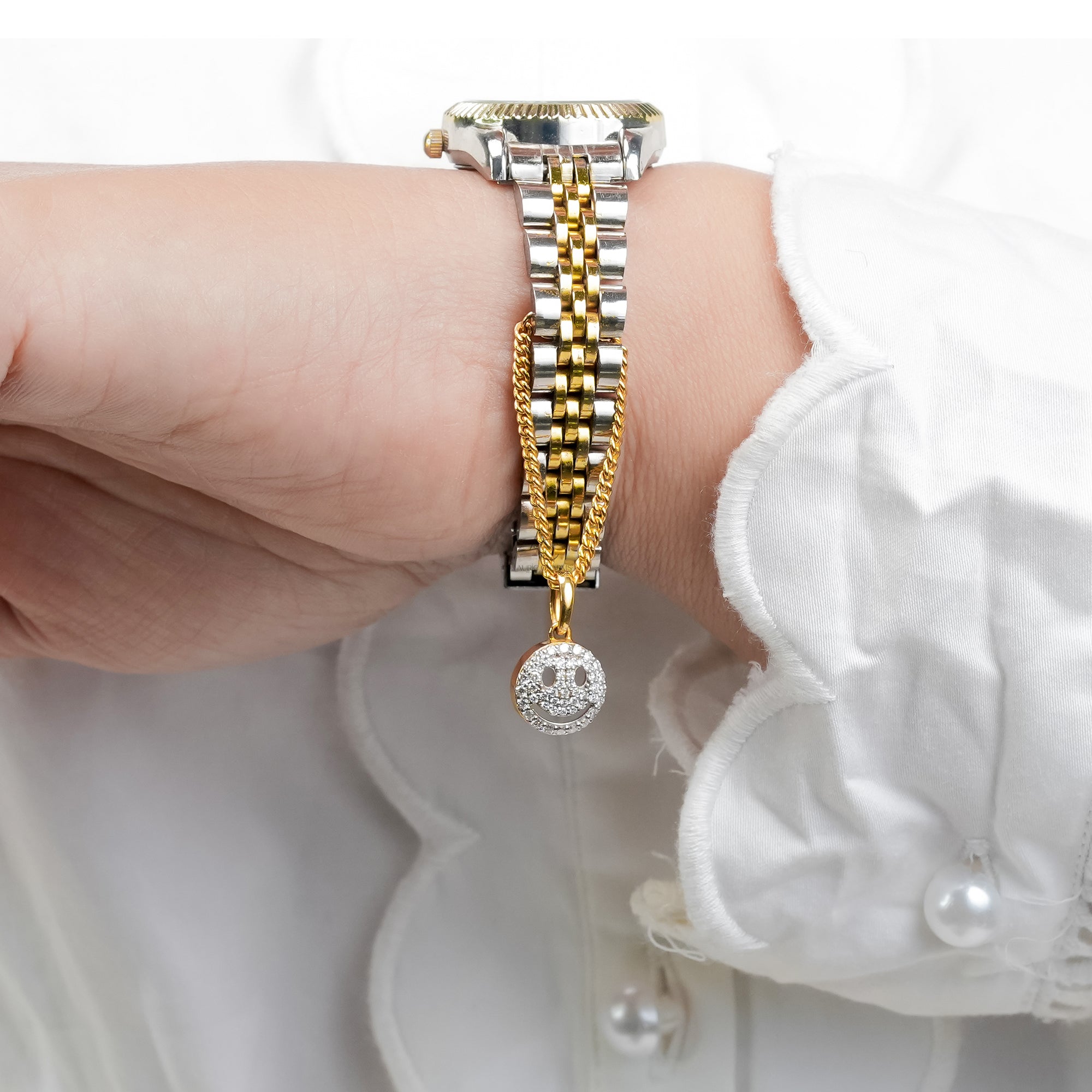 Gold and silver watch with diamond smiley face charm pendant, featuring a gold chain accent for a modern and elegant jewelry-inspired look.