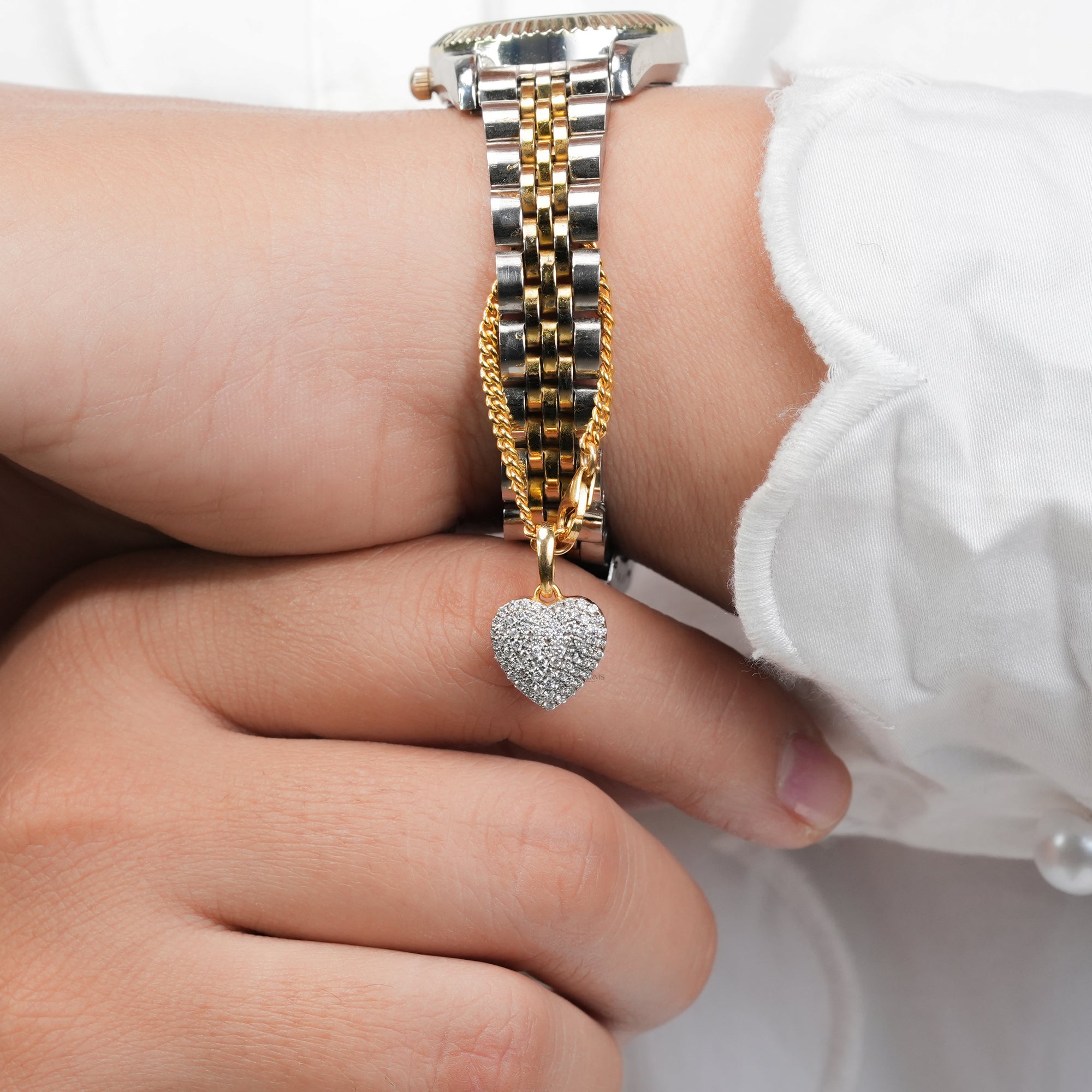 Two-tone metal watch with a gold link accent and a diamond-studded heart charm, displayed on wrist for an elegant and modern presentation.