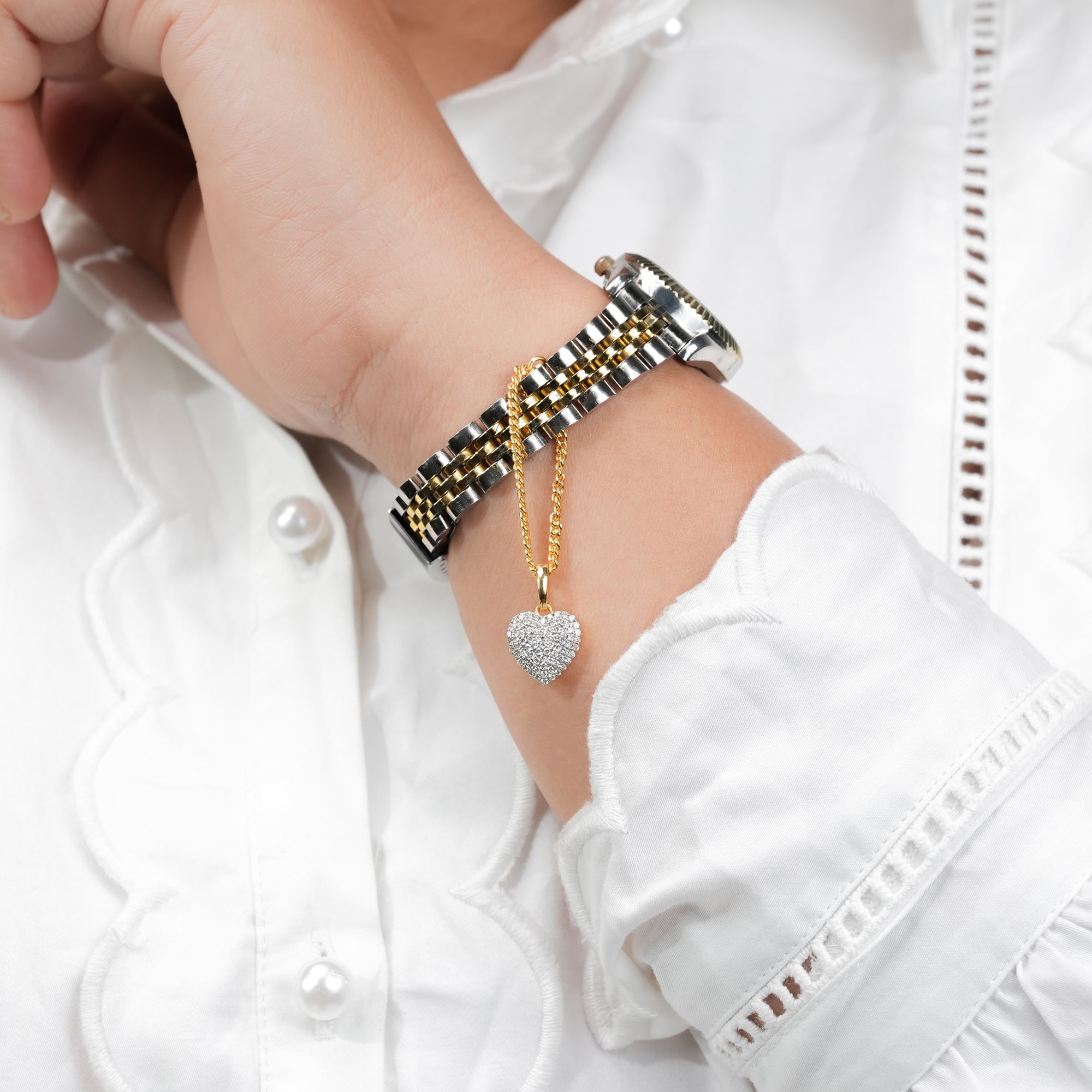 Gold and silver bracelet watch with a diamond heart charm pendant, combining classic watch design with a touch of luxury jewelry detail.