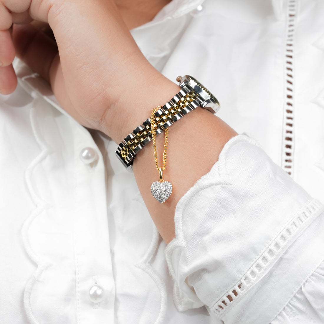 Gold and silver bracelet watch with a diamond heart charm pendant, combining classic watch design with a touch of luxury jewelry detail.