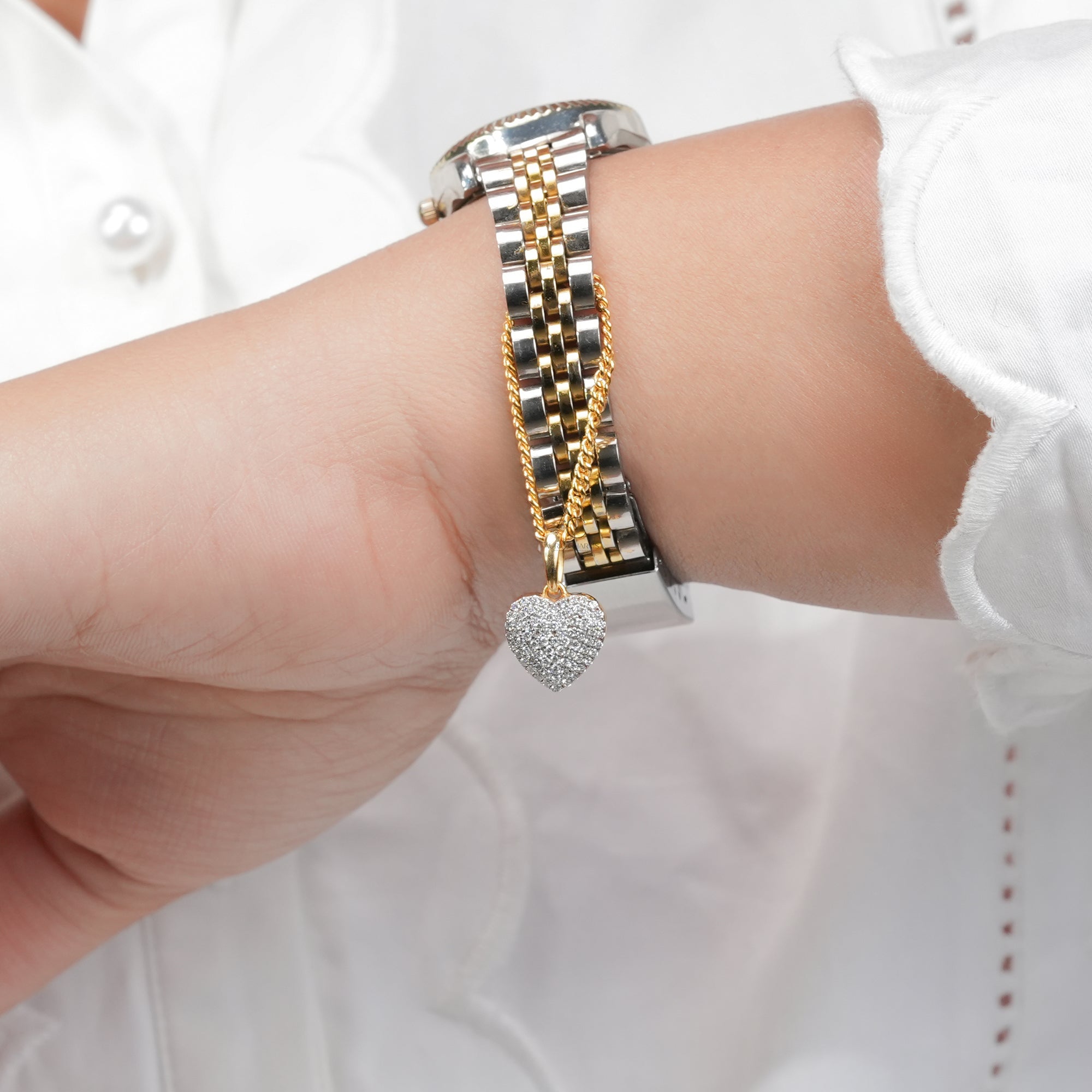 A polished two-tone wristwatch accented with a golden chain and a glittering heart pendant, blending functionality with delicate romantic charm.
