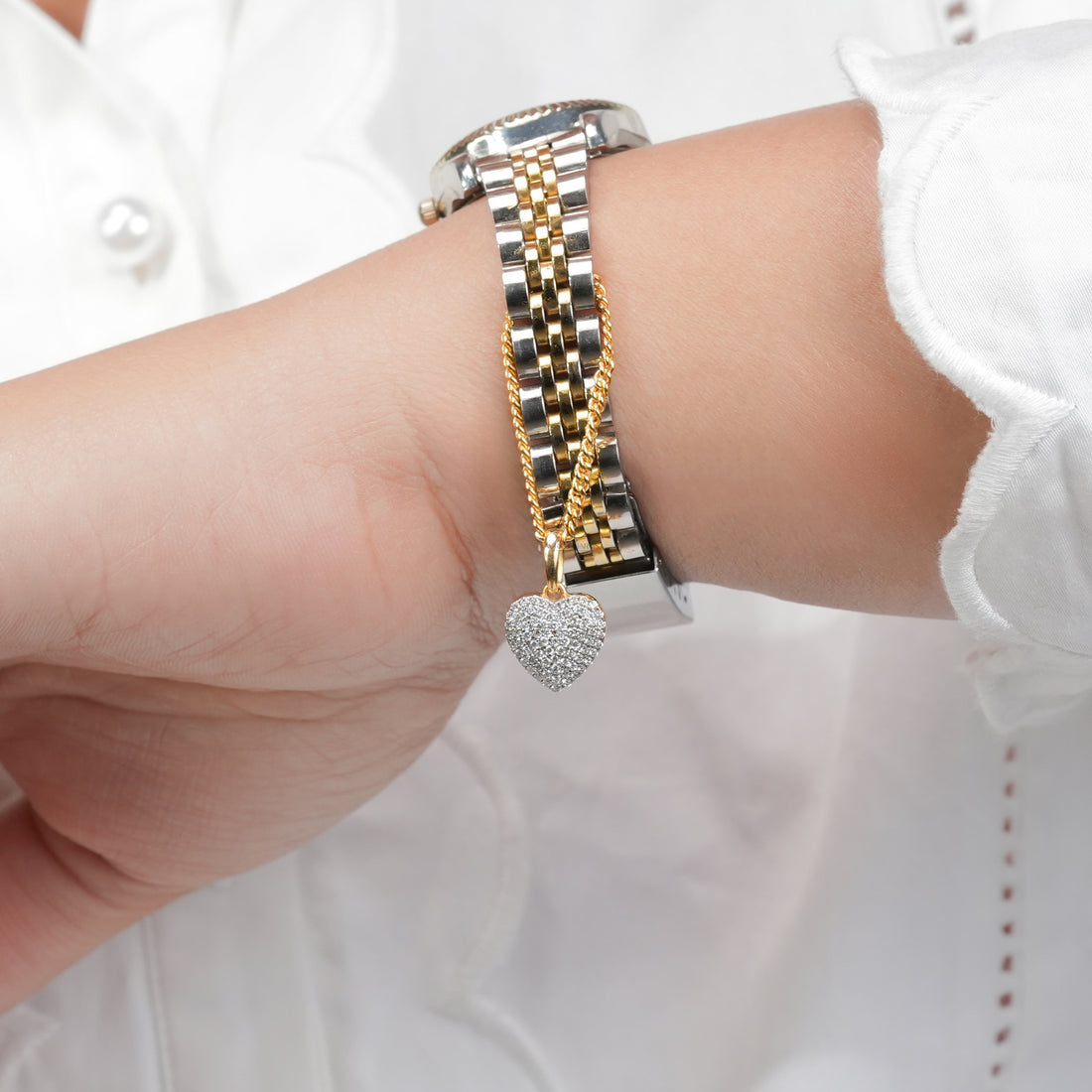 A polished two-tone wristwatch accented with a golden chain and a glittering heart pendant, blending functionality with delicate romantic charm.
