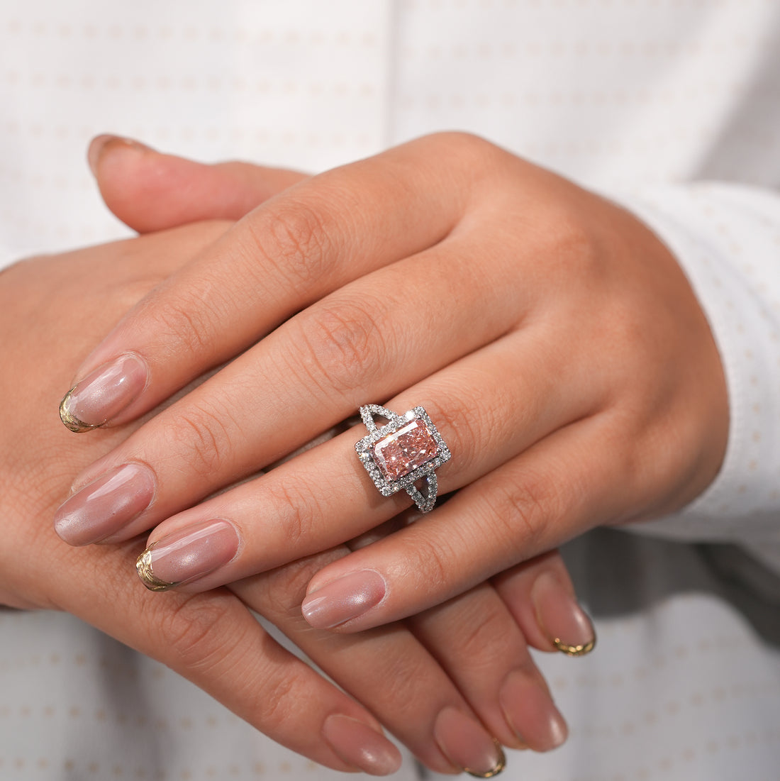 A rectangular pink diamond ring set in a white gold or platinum band, featuring a halo of small white diamonds around the center stone and split shank sides also encrusted with diamonds.