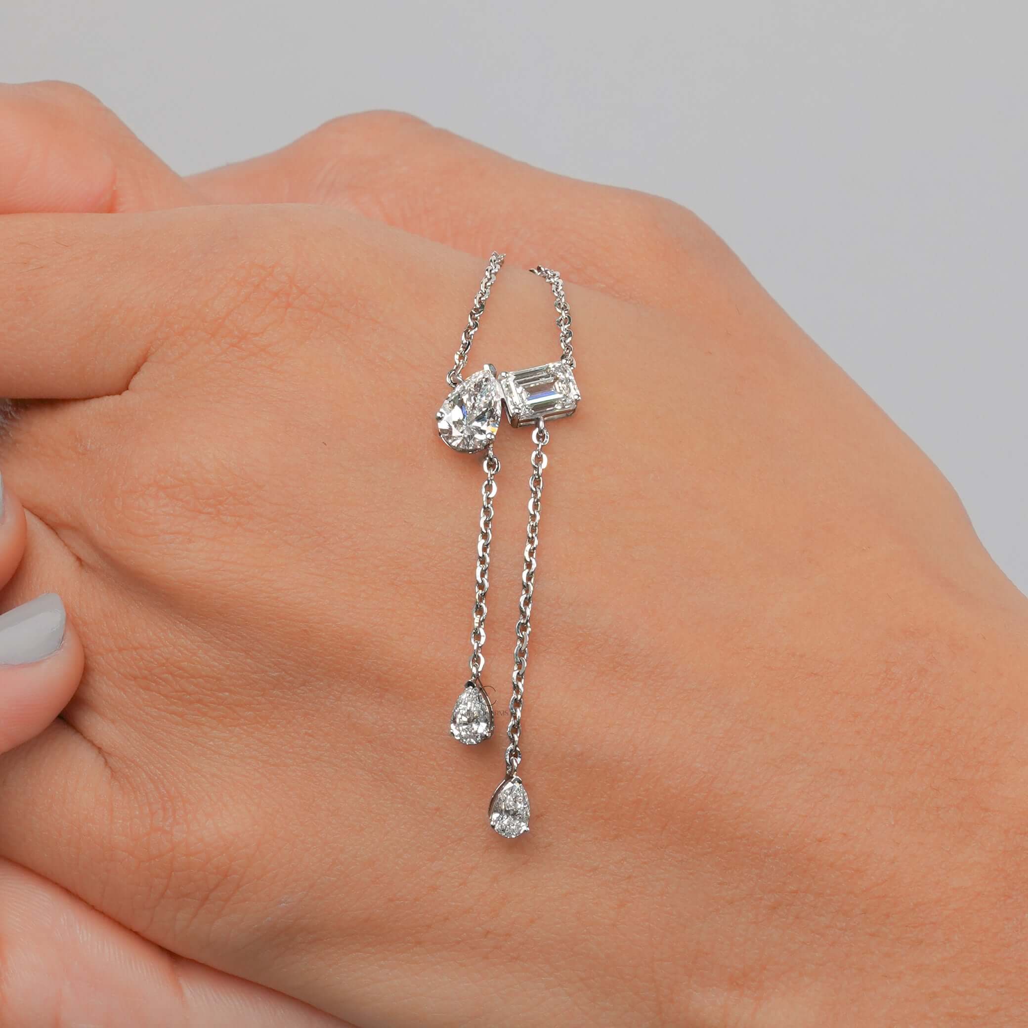 Lab grown diamond Toi et Moi pendant necklace worn on hand, featuring an emerald cut and pearl cut in a luxurious design.