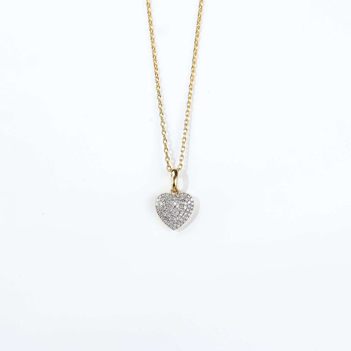 A dainty gold necklace with a diamond heart pendant, illuminated against a deep a sophisticated, high-fashion appeal.