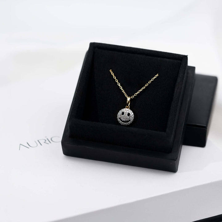A chic gold necklace with a smiley charm encrusted in diamonds, presented against to highlight its brilliance and unique charm.
