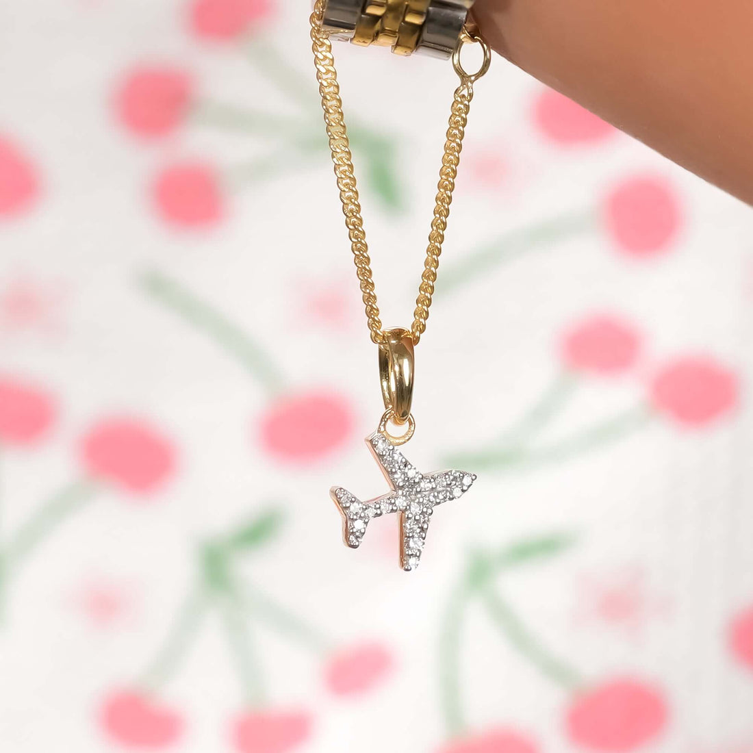 Gold and silver wristwatch with a gold chain and airplane pendant charm encrusted with diamonds a modern, travel-inspired jewelry accessory.