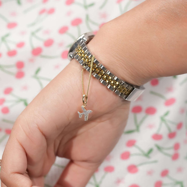 A wrist wearing a two-tone silver and gold bracelet watch, accented with a delicate gold chain featuring a diamond-studded airplane pendant. The sparkling charm adds a playful and elegant touch to the sophisticated timepiece.