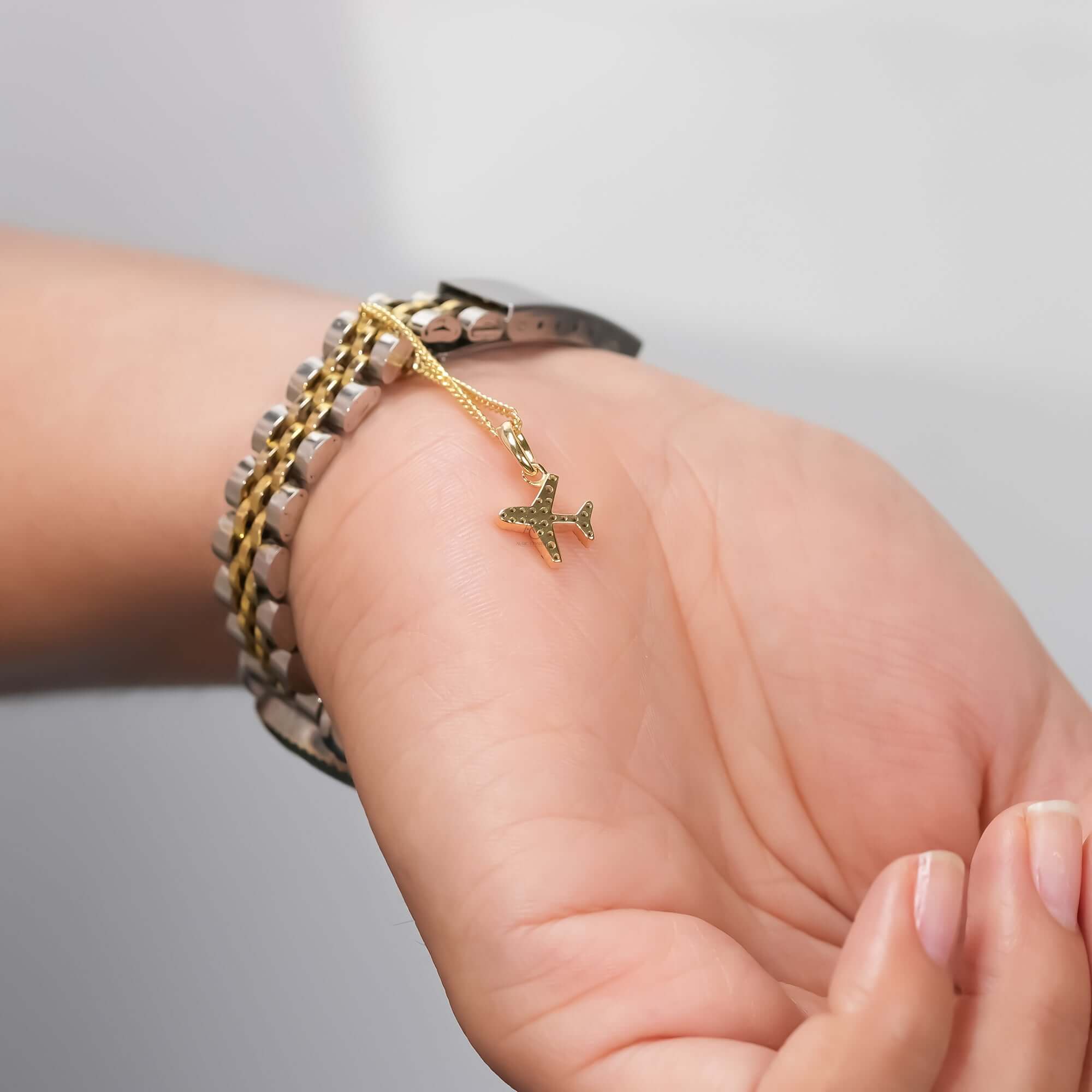 An elegant two-tone wristwatch adorned with a fine gold chain and a shimmering airplane charm in diamonds, blending refined elegance with playful creativity.