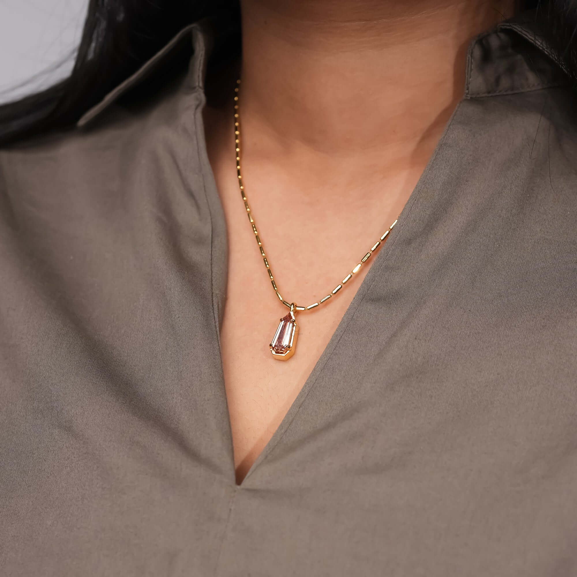 A minimalist gold chain featuring a pale pink gemstone pendant 
