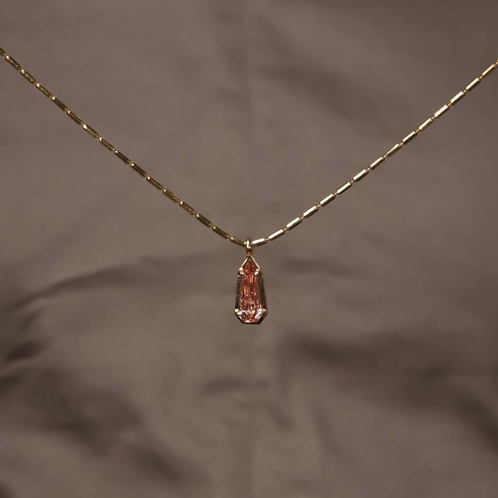 A delicate gold necklace with a pink gemstone pendant, exuding understated elegance and modern sophistication.