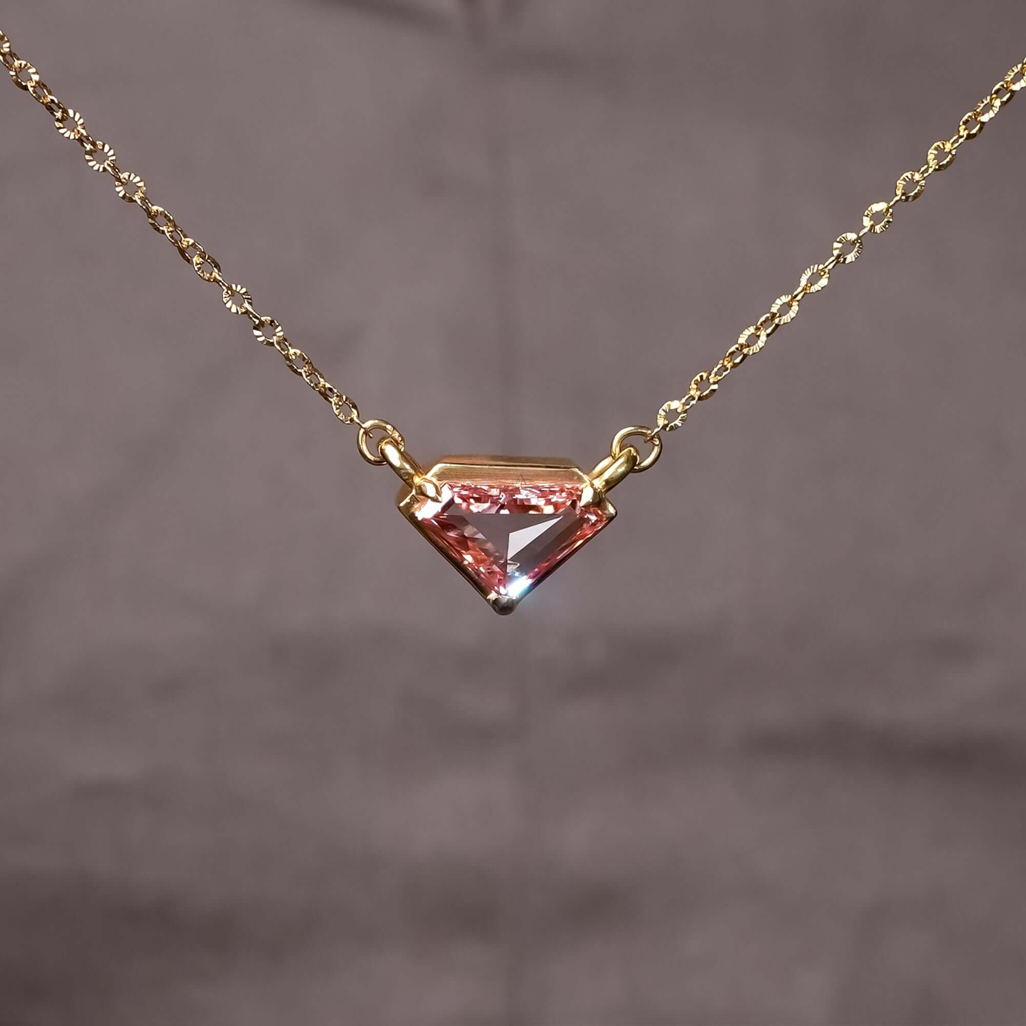 A striking gold necklace featuring a uniquely cut pink gemstone pendant