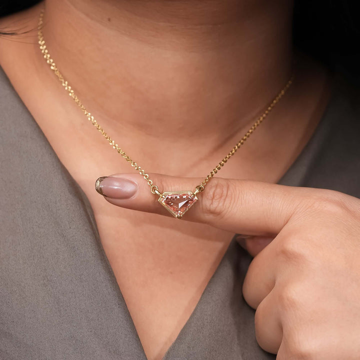 A gold chain necklace featuring a geometric pink gemstone pendant in a kite-cut design.